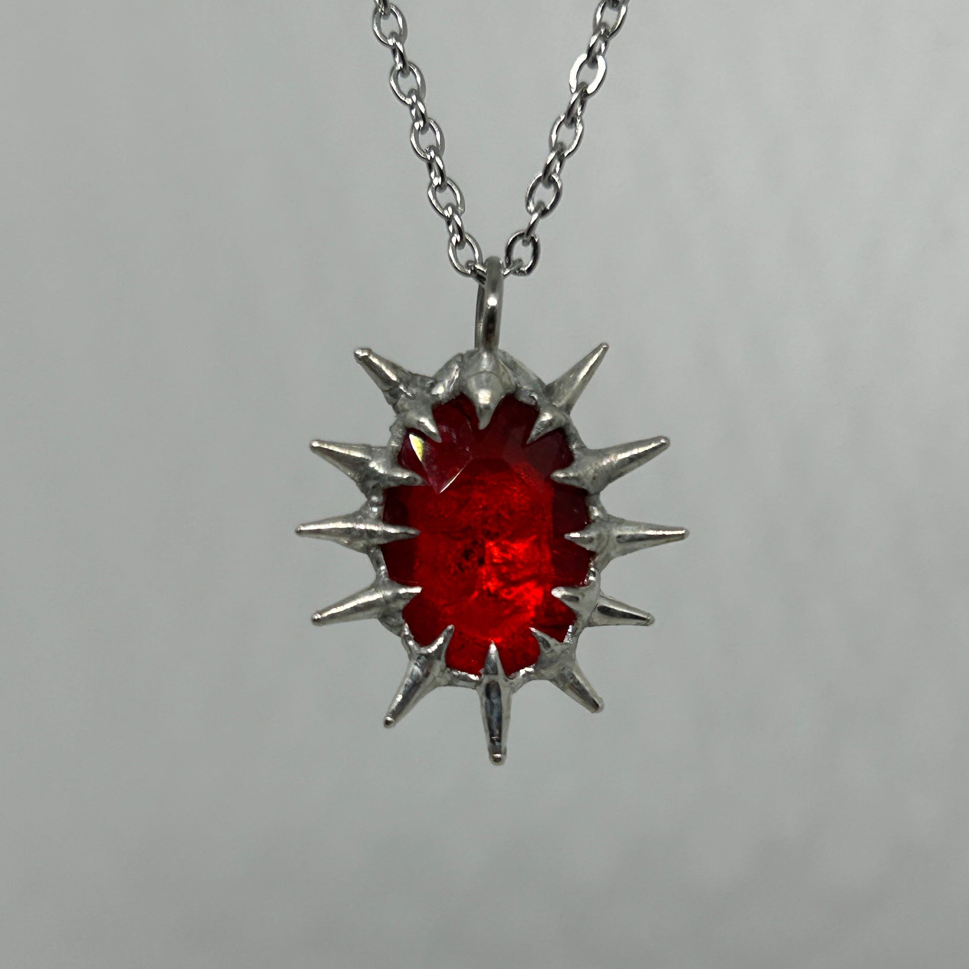 Silver necklace with a red spiky pendant on a gray background