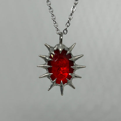 Silver necklace with a red spiky pendant on a gray background